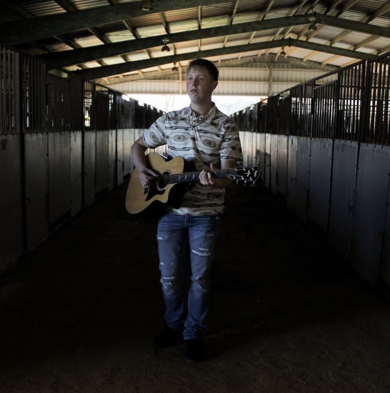 Bryce Blackwell with his guitar in a stable aisle